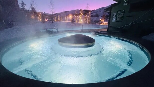 Una vasca idromassaggio dalla forma circolare, circondata dalla neve e illuminata da luci soffuse.