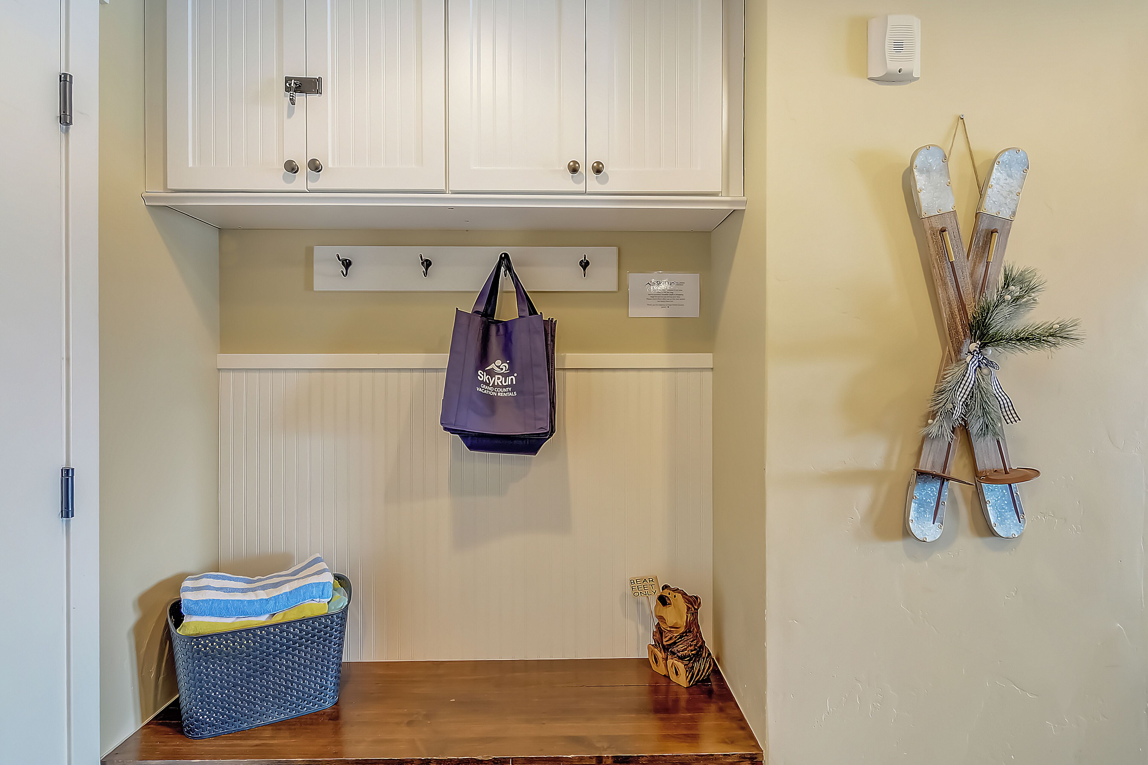 A wooden bench with a basket, a hanging bag, and a decorative item on the wall.
