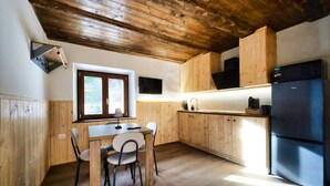 Eine Küche mit Holzausstattung, einem Esstisch mit Stühlen, einem Kühlschrank und einem Fenster mit Tageslicht.