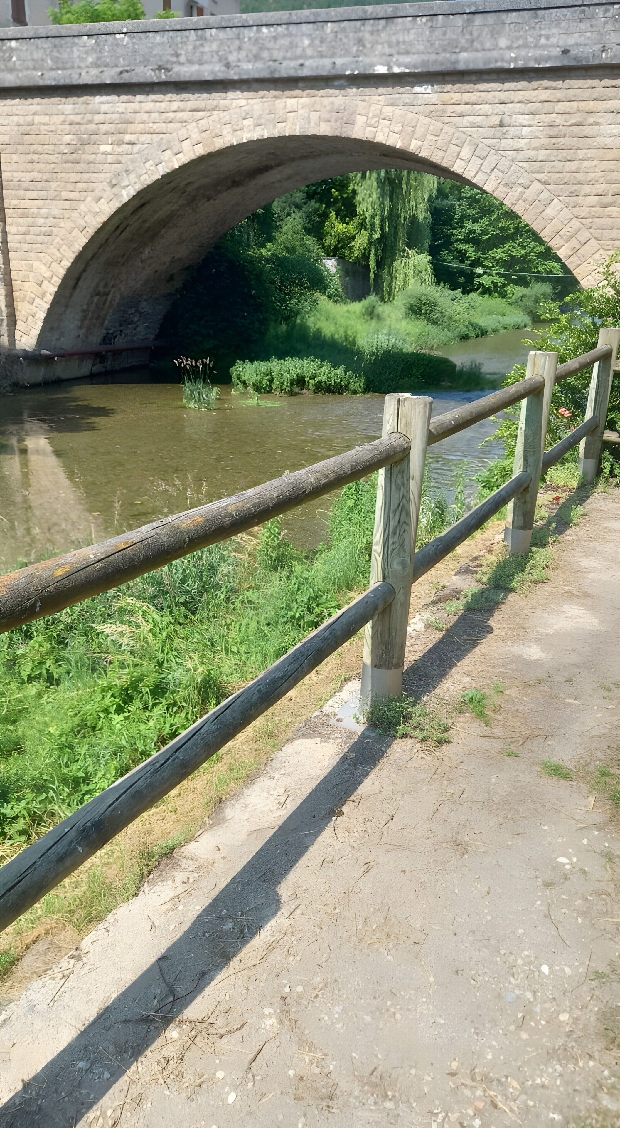Eine Steinbrücke über einem Fluss mit Holzzaun und grünen Ufern.