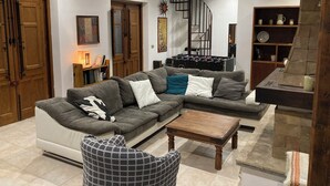 Een moderne woonkamer met een grijze modulaire bank, een houten salontafel en een tafelvoetbalspel. Er is een trap met een zwarre leuning die naar een hoger gelegen verdieping leidt.
