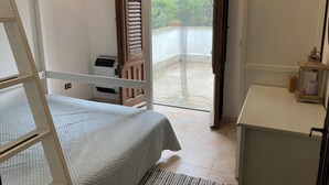 Een kamer met een stapelbed, een bureau, een kleine tafel met een lantaarn en uitzicht op de natuur via een schuifdeur.