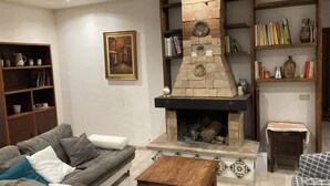 Een woonkamer met een stenen open haard, een grijze bank, een houten salontafel en boekenkasten.