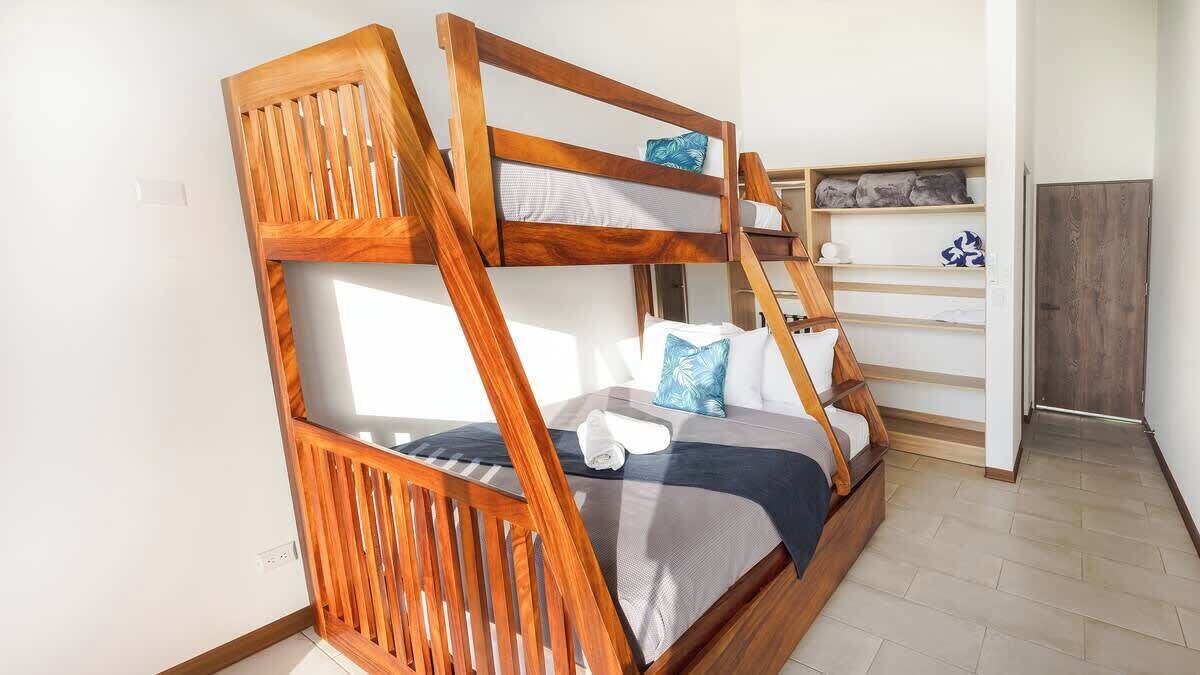 Una cama individual con barandillas de madera, una pared blanca y un estante con toallas.