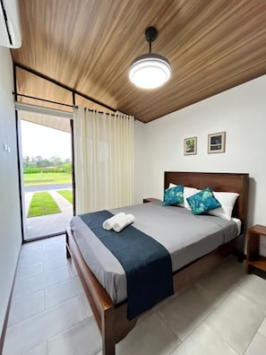 A bedroom with a bed, a nightstand, a ceiling light, and a view of the outdoors. - Colibri Villas del Bosque at La Fortuna (La Fortuna)