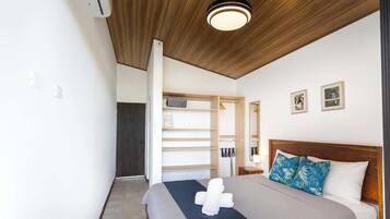 Ein Schlafzimmer mit einem Bett, einem Holz-Kopfteil, einem Nachttisch, einem Wandspiegel und einem eingebauten Kleiderschrank mit Regalen.