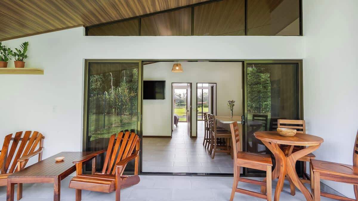 Un comedor moderno con muebles de madera, grandes puertas correderas de vidrio que dan a un espacio exterior y un televisor de pantalla plana montado en la pared.
