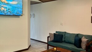 Een woonkamer met een houten plafond, een flatscreen-televisie, een groene bank, een houten salontafel en een houten vloer.
