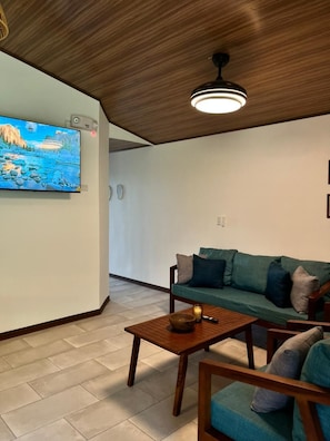 Un salon avec un plafond en bois, un téléviseur à écran plat, un canapé vert, une table basse en bois et un plancher en bois.
