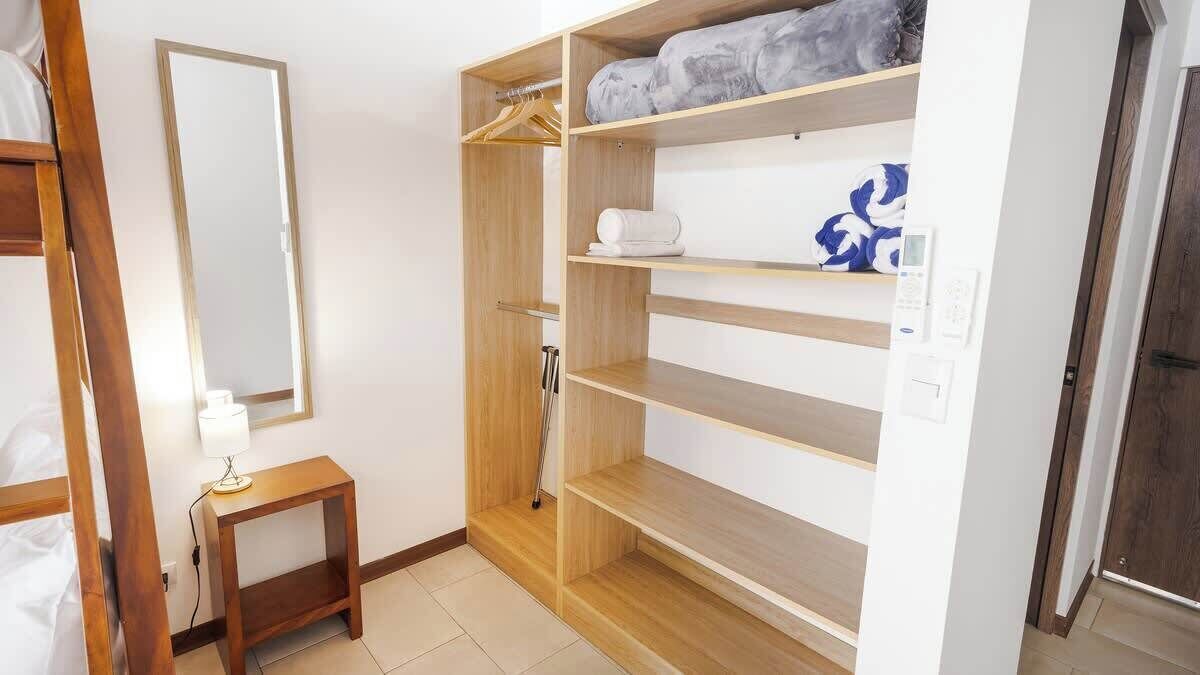 Habitación de hotel con un armario de madera, una mesita de noche con lámpara y un espejo.