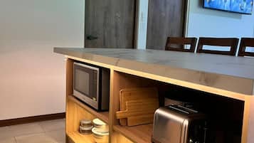 Una cocina compacta con microondas, tostadora y sartén sobre una estante de madera.