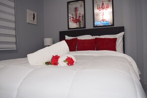 Een net opgemaakt bed met wit en rood beddengoed, een opgerold wit kussen en een boeket rode bloemen.