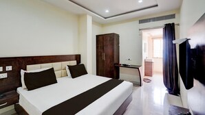 Een hotelkamer met een groot bed, een kledingkast, een bureau met een computer en een badkamer die door een open deur zichtbaar is.