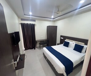 A hotel room with a bed, a desk, a chair, a wardrobe, and a ceiling fan. - Townhouse Kanithi Road (Visakhapatnam)