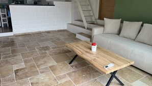 Uma sala de estar com sofá, mesa de centro de madeira e cozinha ao fundo.