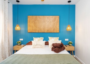 Een slaapkamer met een groot bed, twee nachtkastjes, een kunstwerk aan de muur en twee hanglampen.