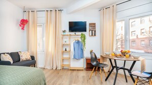 Quarto moderno com uma cama, uma escrivaninha com cadeira, uma televisão e janela com vista para edifícios.