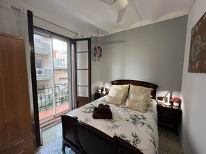 Ein Schlafzimmer mit Bett, Nachttisch, Fenster mit Blick auf Gebäude und einer Tür zum Balkon.