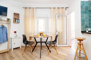 Eine moderne Küche mit Esstisch, Stühlen, einem kleinen weißen Schrank, einer hängenden Pflanze und einem Fernseher an der Wand.