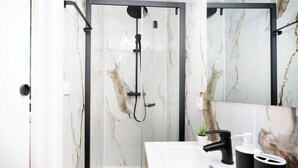 Ett modernt badrum med en duschkabin i glas, en vit tvättställ med svarta detaljer och väggar med marmorliknande mönster.