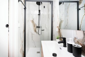 Ein modernes Badezimmer mit Duschkabine aus Glas, einem weißen Waschbecken mit schwarzen Armaturen und Wänden mit Marmormuster.