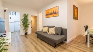 Ein modernes Wohnzimmer mit einem grauen Sofa, einem Esstisch mit Stühlen, einer Zimmerpflanze und einem Bild an der Wand.