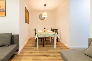 A dining area with a table set for four, a clock on the wall, and a sofa on the left. - Apart. 3 bedr. 8'. Fira Barcelona and 20' Bcn center (L'Hospitalet de Llobregat)