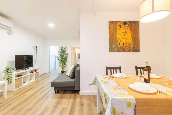 A modern living room with a flat-screen TV, a sofa, a dining table set for two, and a painting on the wall. - Apart. 3 bedr. 8'. Fira Barcelona and 20' Bcn center (L'Hospitalet de Llobregat)
