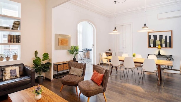 A spacious living area with a dining table, chairs, and a kitchen in the background. - Apartment Luxe Gran Via 5 Bedrooms - 8 min Paseo Gracia (Barcelona)