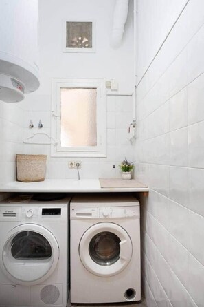 A laundry room with two front-loading washing machines, a small sink, and a window above the machines. - Apartment Luxe Gran Via 5 Bedrooms - 8 min Paseo Gracia (Barcelona)