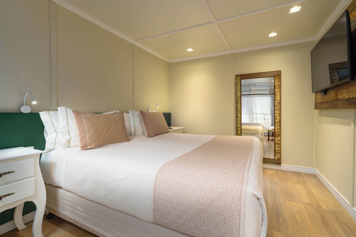 Una habitación de hotel con una cama grande, mesitas de noche, un espejo y un televisor.