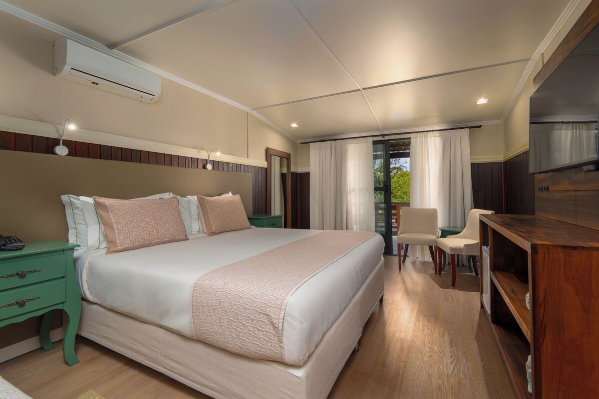 Una habitación de hotel con una cama grande, mesitas de noche, un escritorio y un espejo.