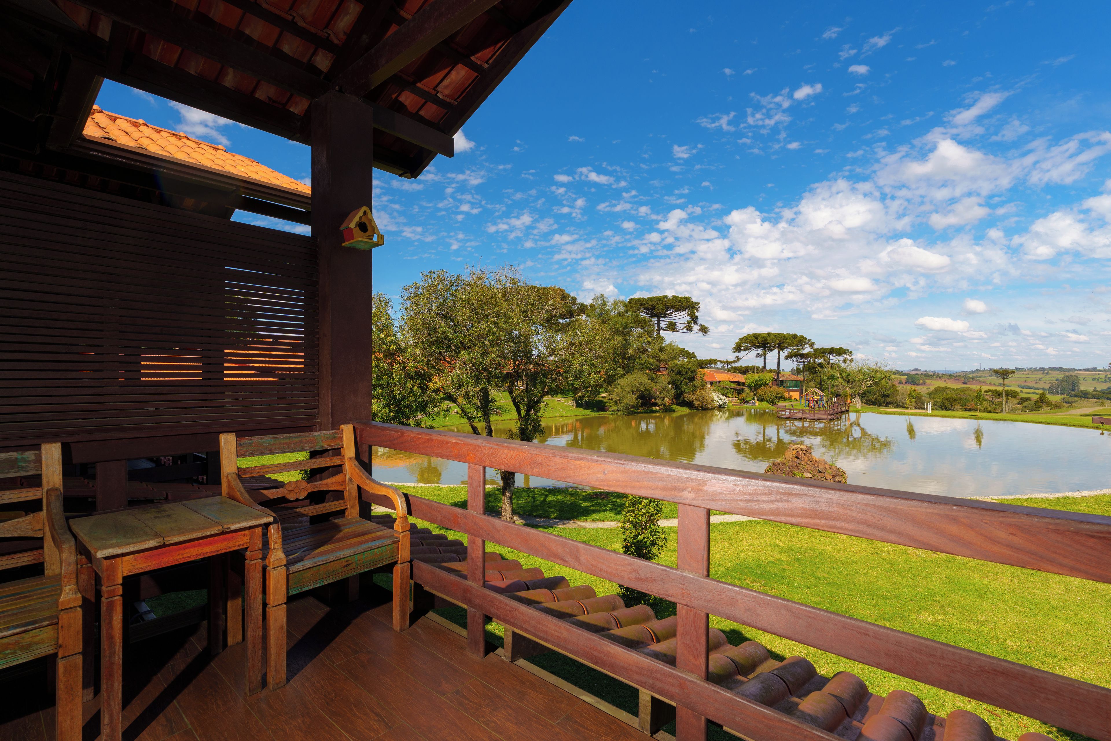 A wooden deck with a view of a lake, trees, and a distant building.