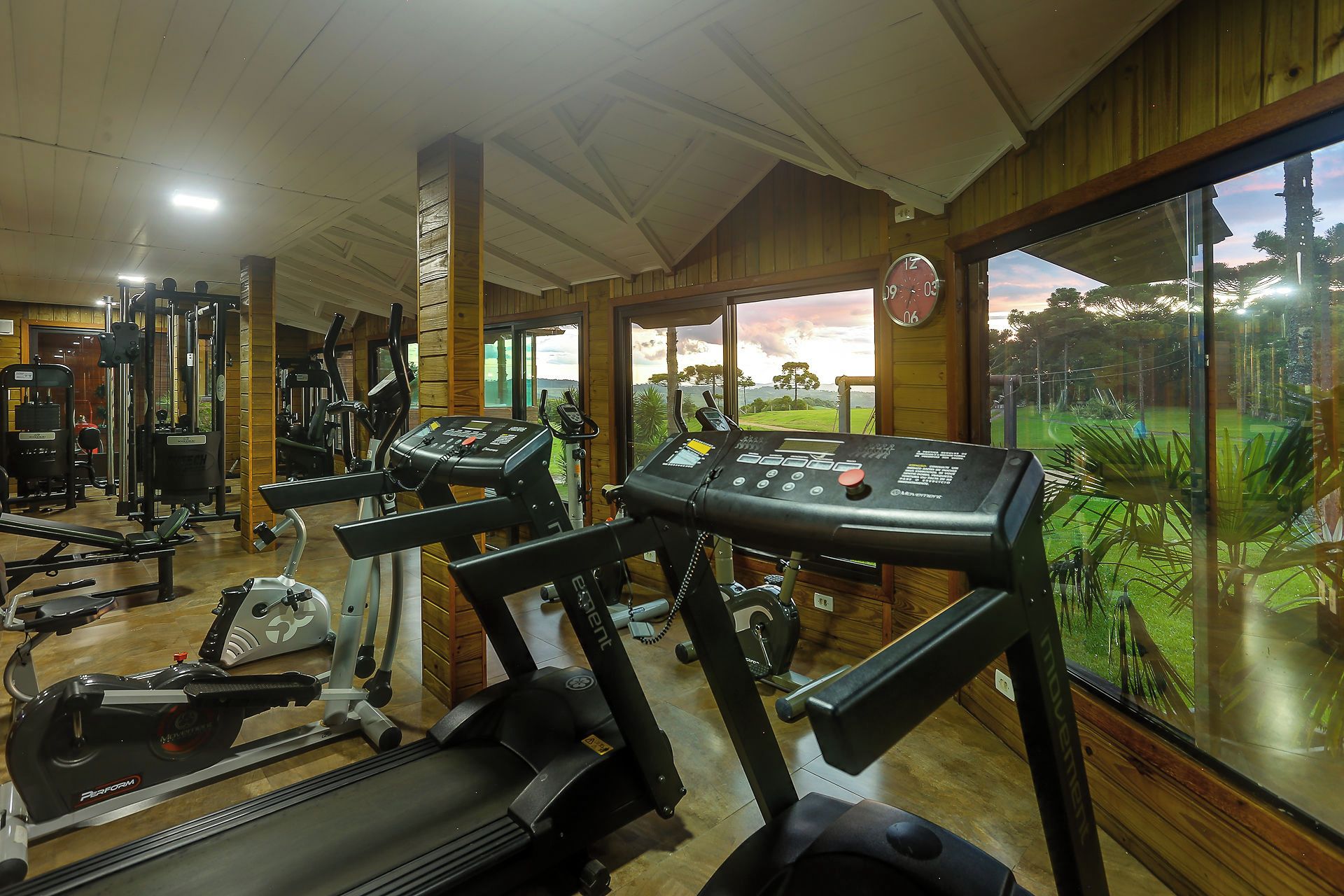 A gym with various exercise equipment, large windows, and a view of the outdoors.