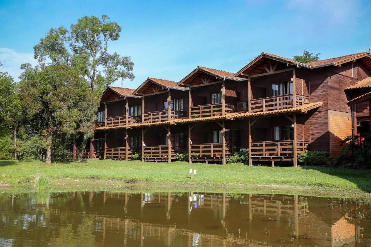 Een rij houten bungalows met balkons, een vijver op de voorgrond en bomen op de achtergrond.