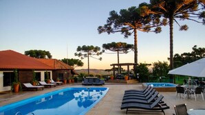 Una piscina con sillas de descanso, un área de estar techada y altos árboles.