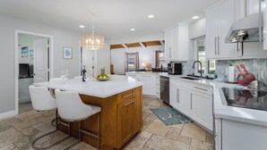 Una cocina moderna con armarios blancos, una isla central con taburetes y una lámpara colgante, además de un revestimiento de azulejos.