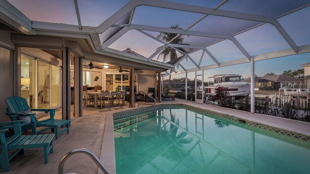 Una piscina interior con techo de vidrio, zona de estar y vista hacia un puerto deportivo.