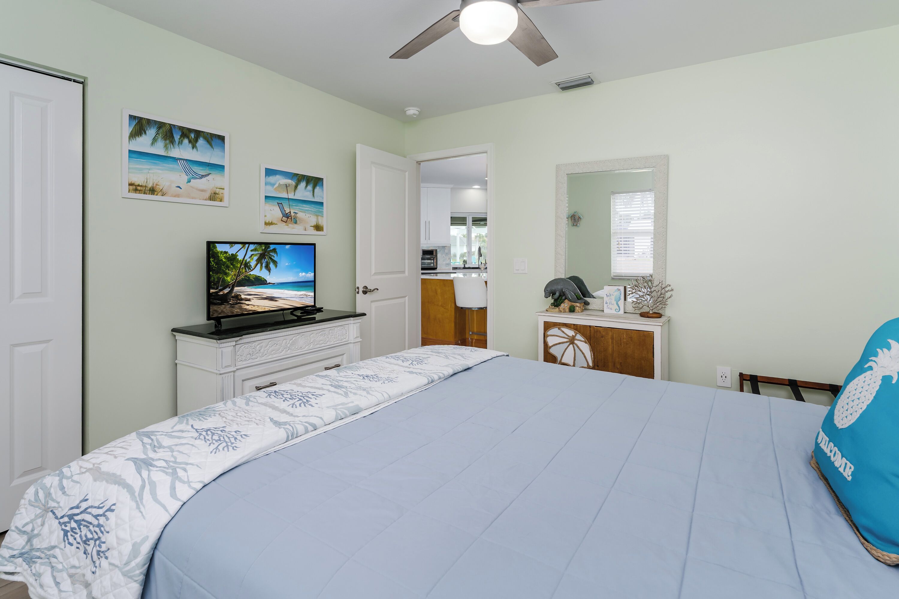 Une chambre à coucher comprenant un lit, une télévision, un ventilateur de plafond et une porte donnant sur une salle de bain.