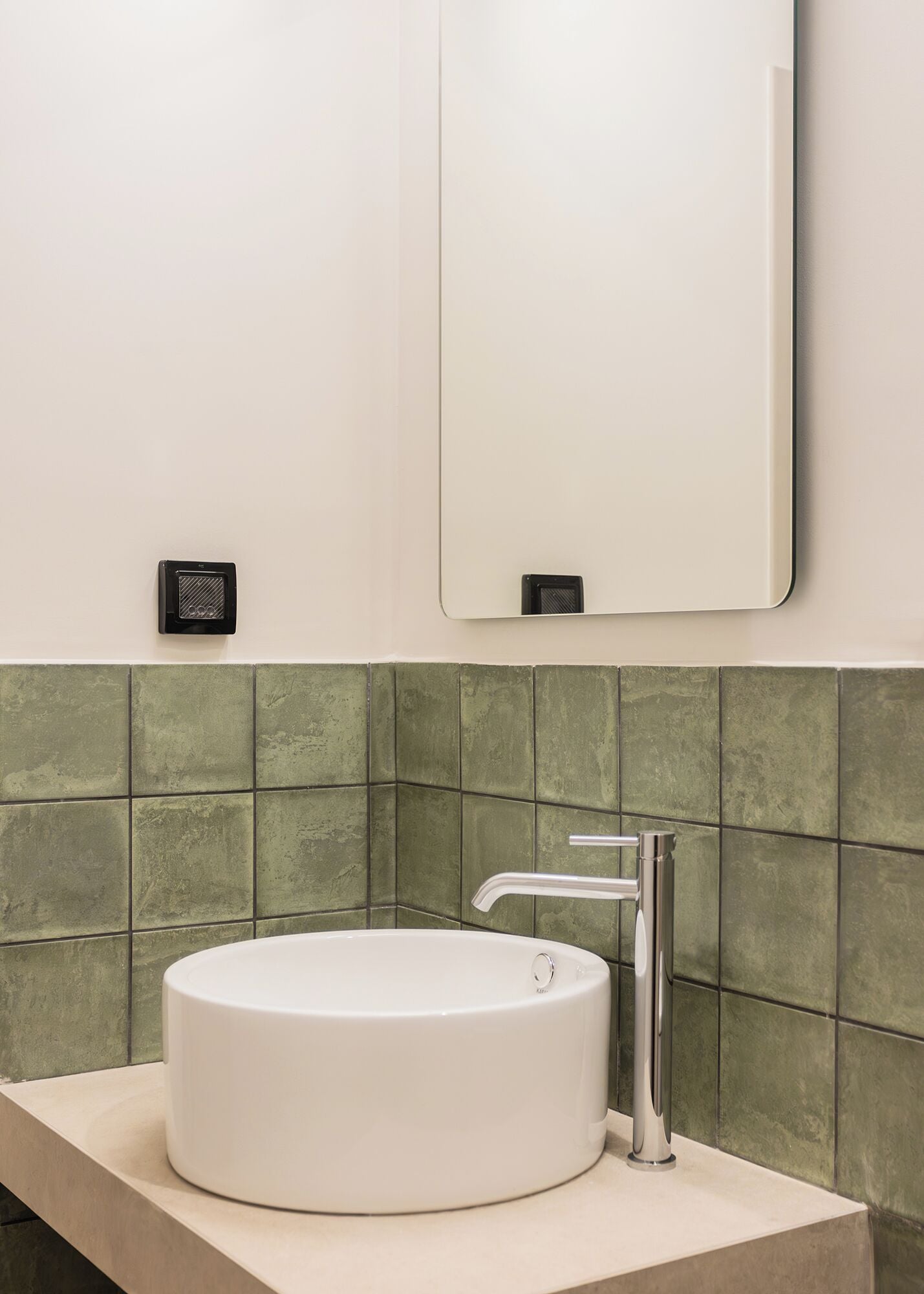 A bathroom with a round sink, a mirror, and green tiled walls.