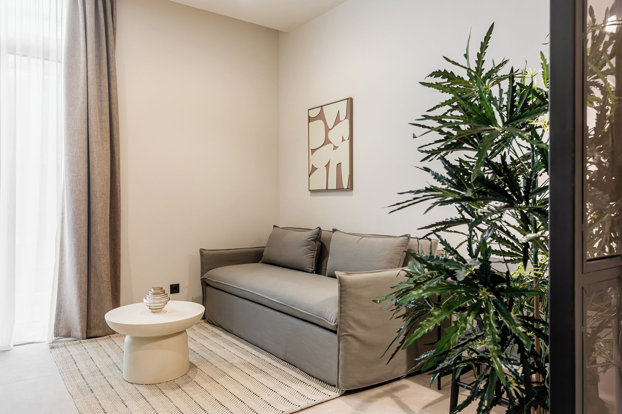 A modern living room with a grey sofa, a small round table, and a large green plant.