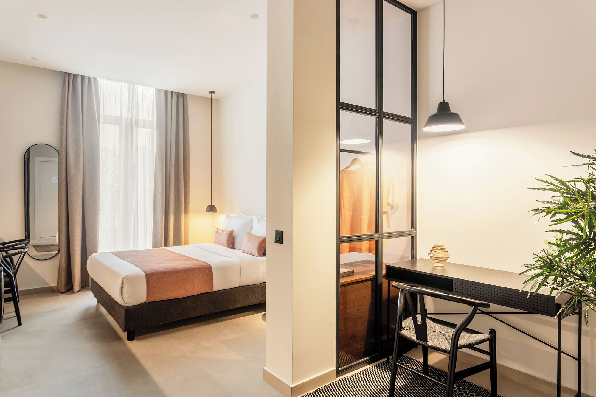 Camera d'albergo moderna con un letto, una scrivania, una sedia, uno specchio e una pianta.