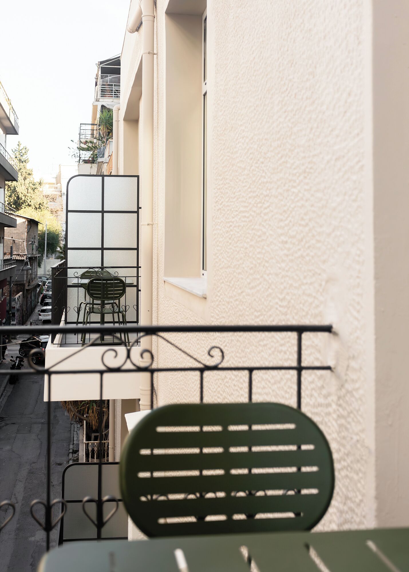 Ein Balkon mit einem grünen Stuhl, einem kleinen Tisch und einem Fenster mit Blick auf eine Straße.