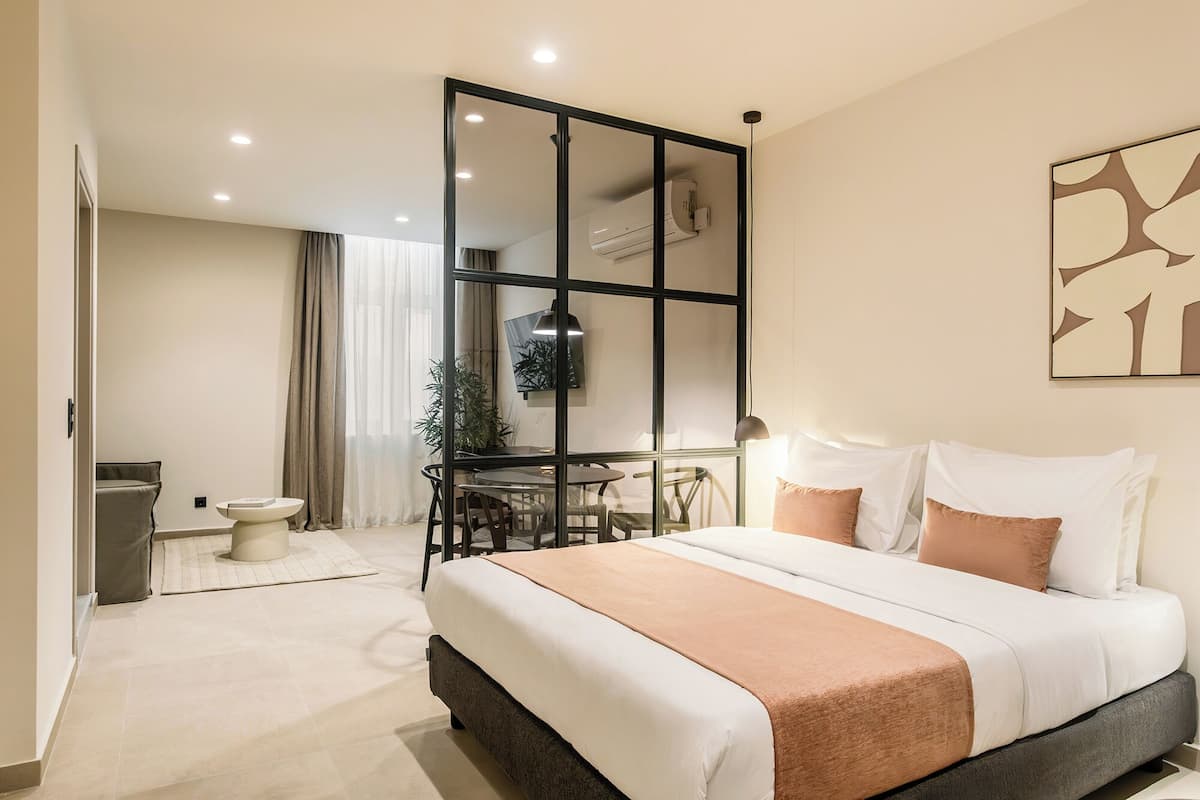 A modern hotel room with a large bed, a dining area, and a separate bathroom.
