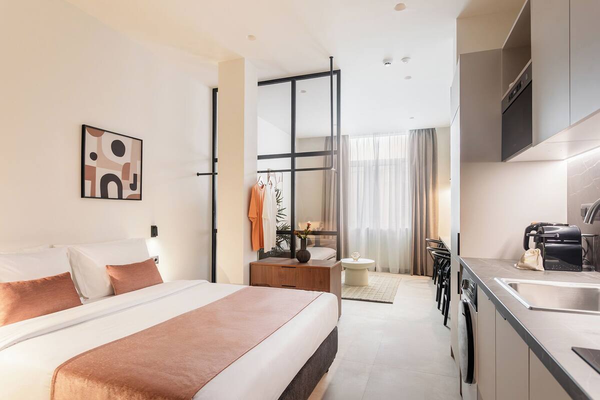 A modern hotel room with a large bed, a kitchenette, and a bathroom.