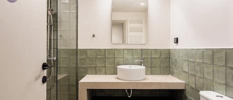 A bathroom with a glass shower enclosure, a sink with a mirror above it, and a toilet.