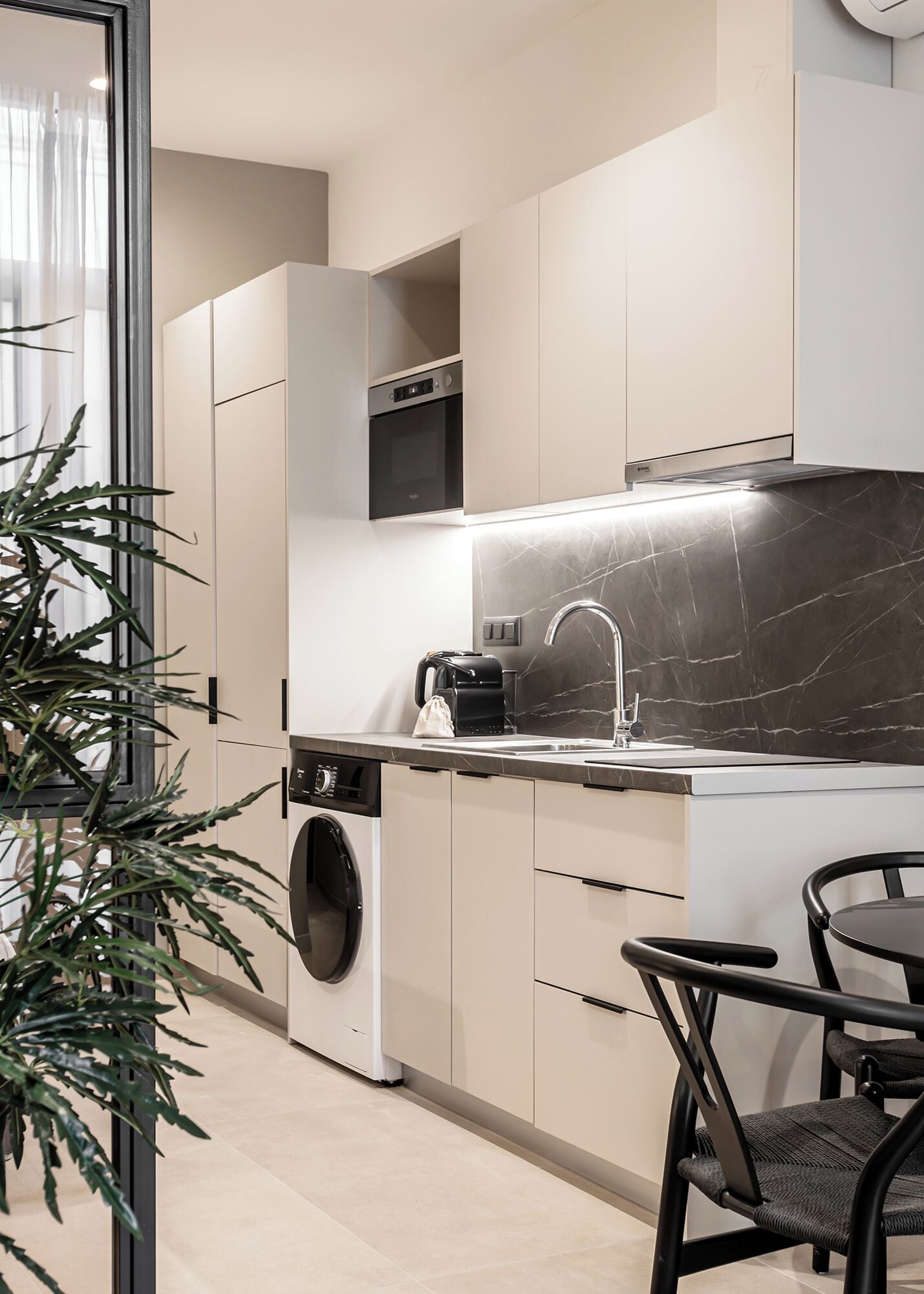 A modern kitchen with built-in appliances, a sink, and a dining area with chairs.