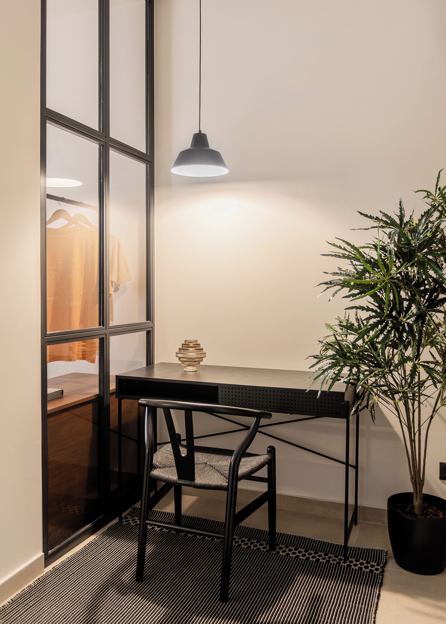 Et lille værelse med et bord, en stol, en hængende lampe og en potteplante.