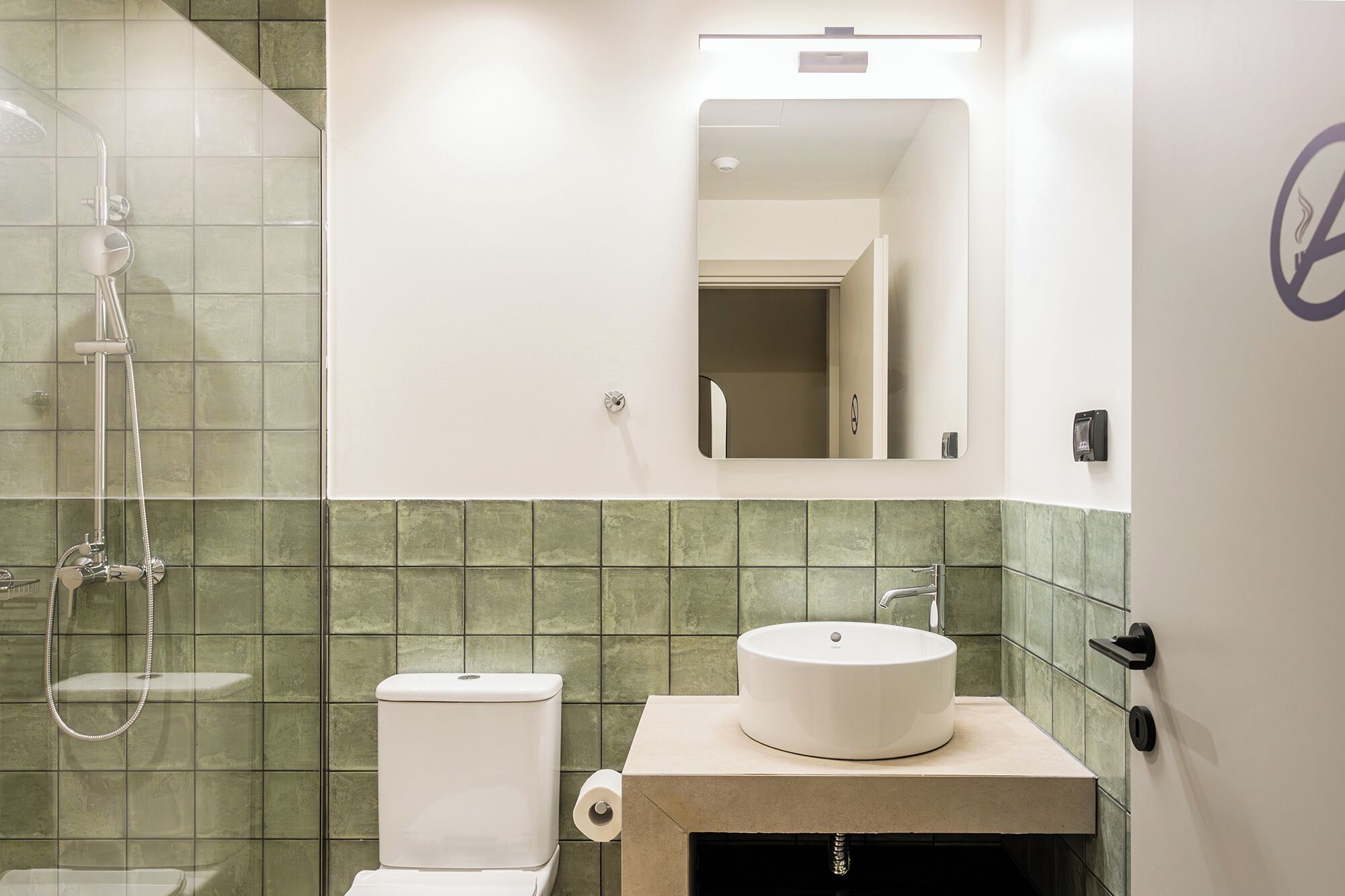 A bathroom with a shower, toilet, and sink, featuring green tiles and a mirror.