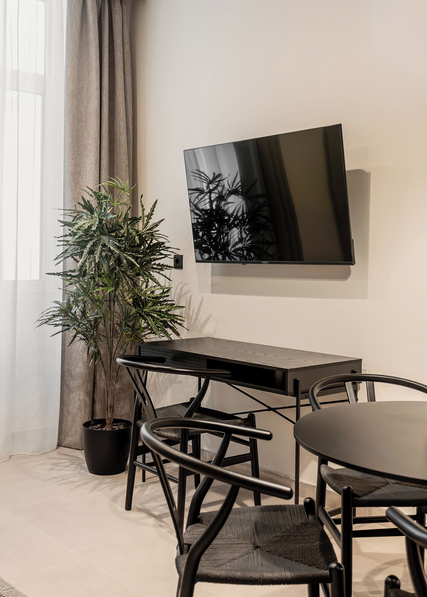 Una habitación moderna con un televisor negro en la pared, una planta en maceta, una mesa negra y dos sillas.